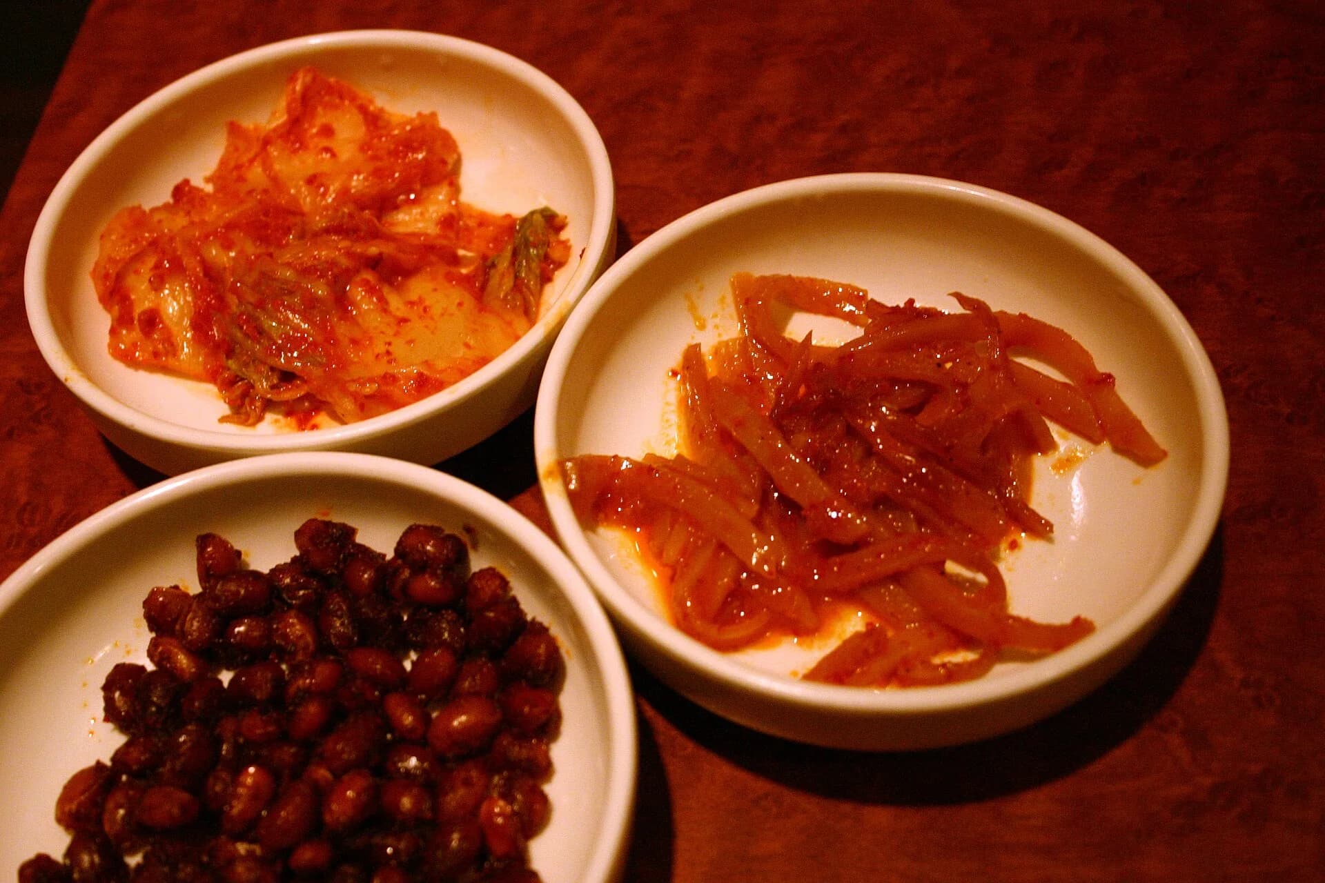 Small Korean side dishes including kimchi, beans and seasoned dried squid
