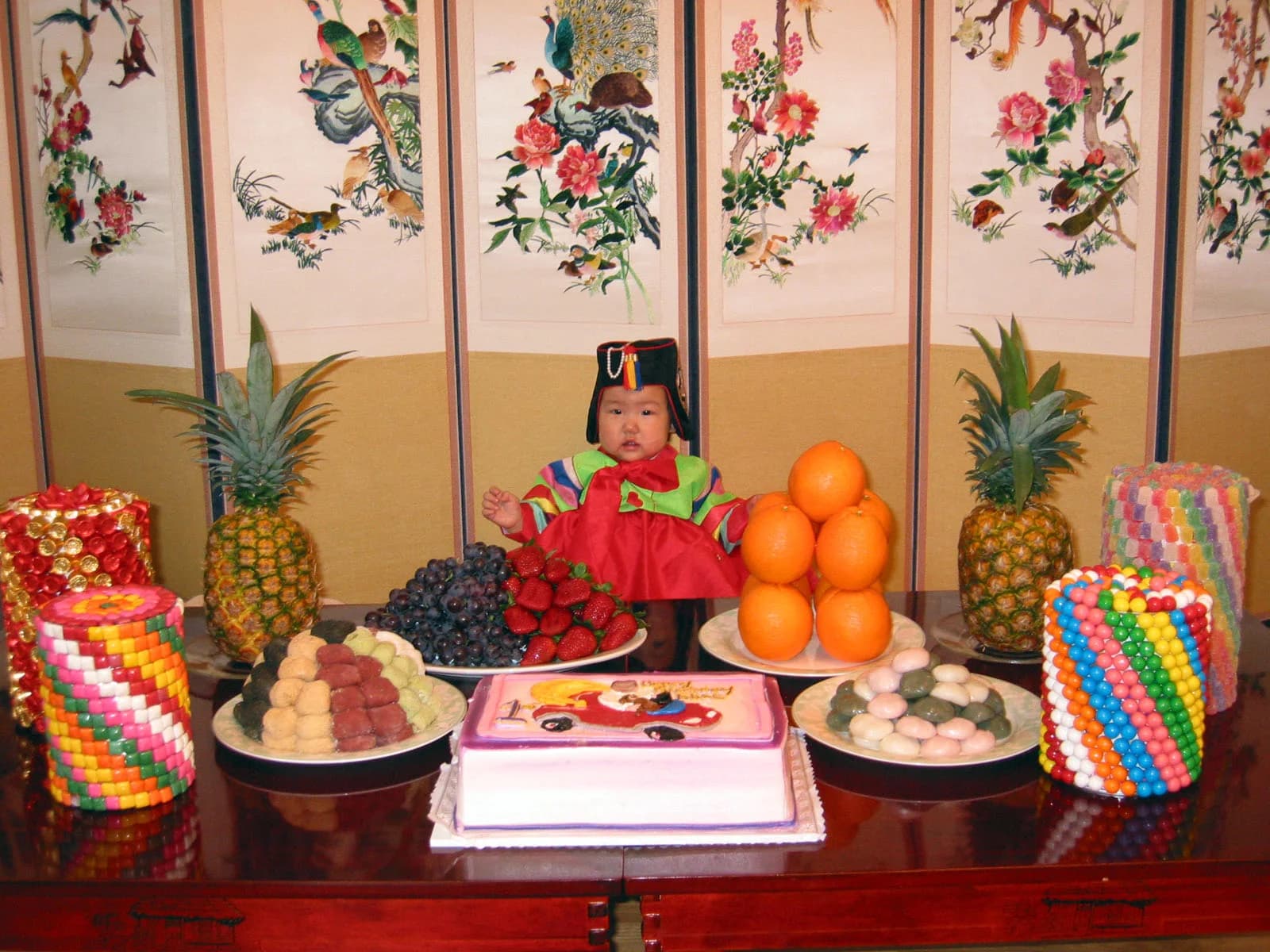A baby in hanbok beside rice cakes at a Korean first-birthday celebration