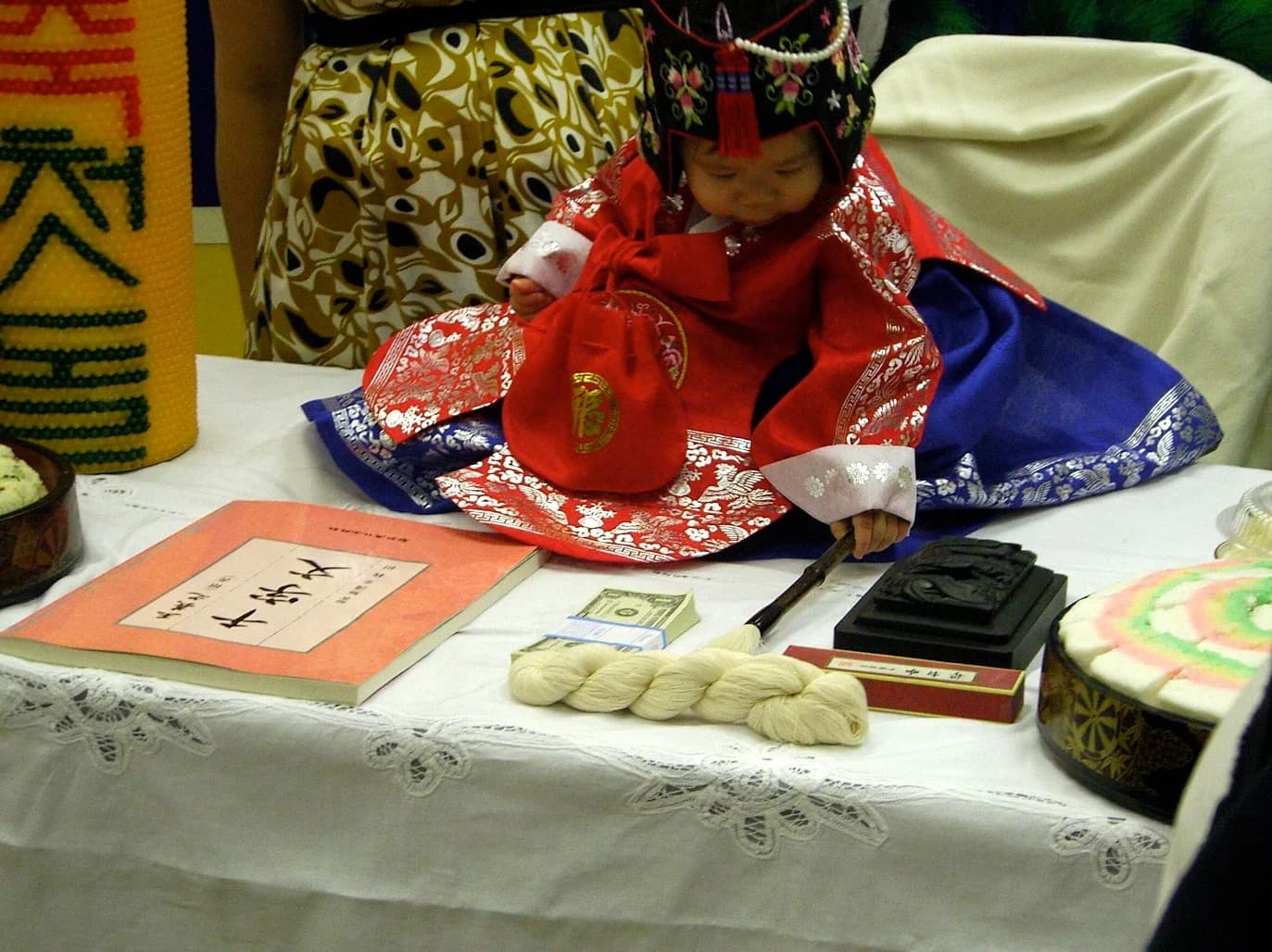 A child in hanbok seated at a Korean first-birthday celebration