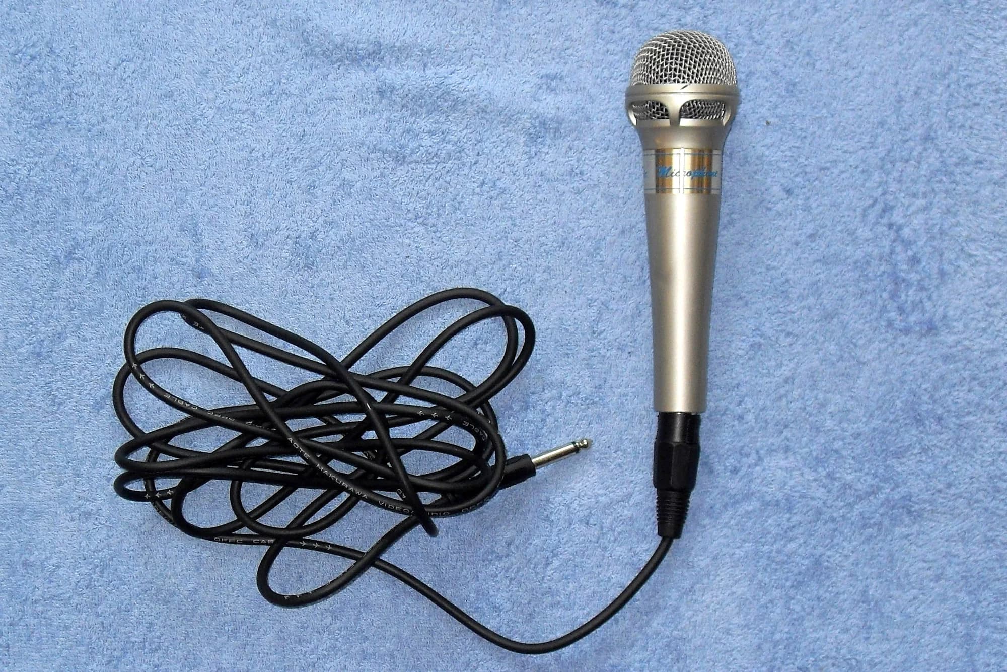 A wired karaoke microphone resting on blue fabric
