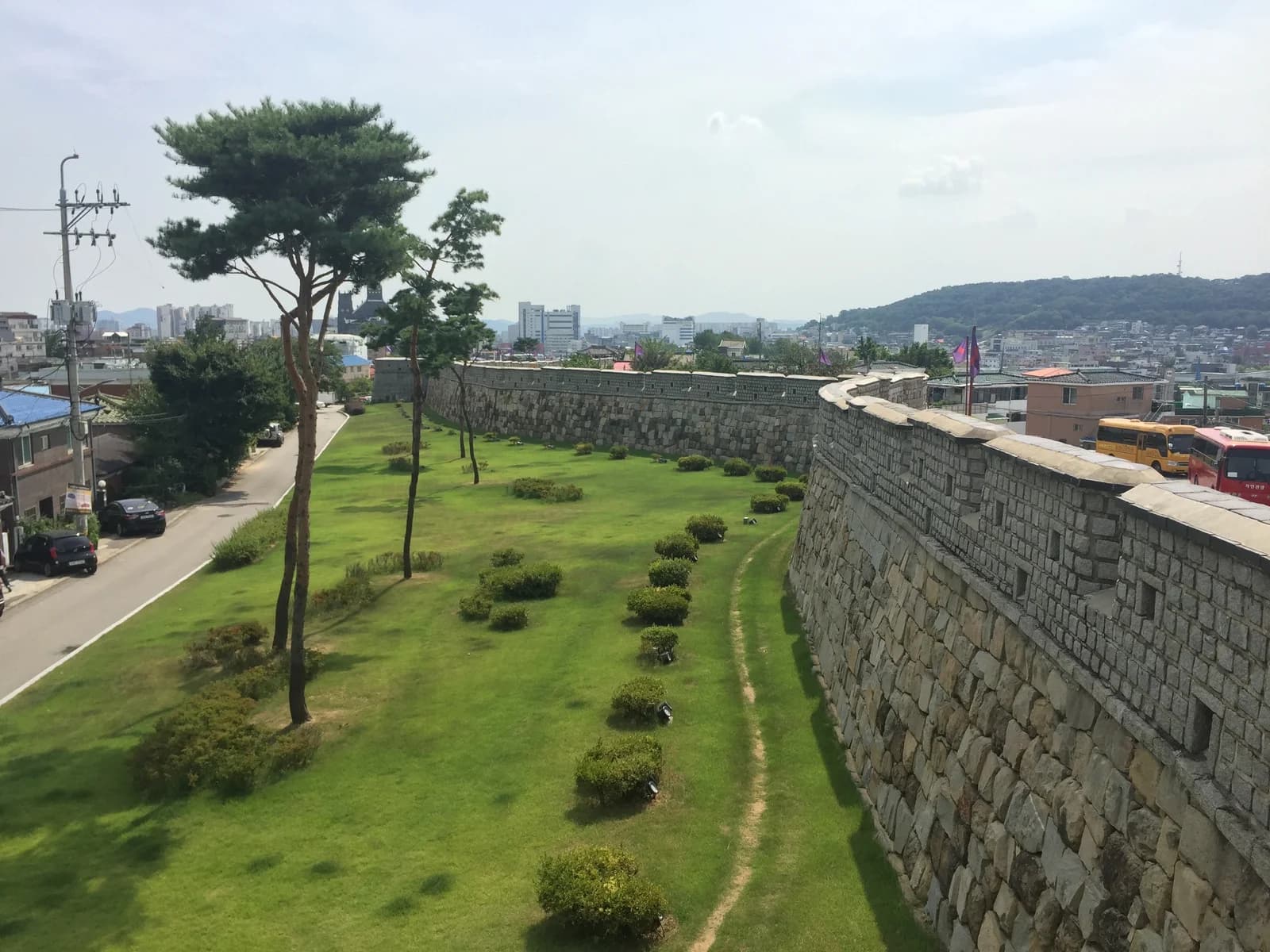 A curving section of Suwon Hwaseong stone wall beside streets and city buildings