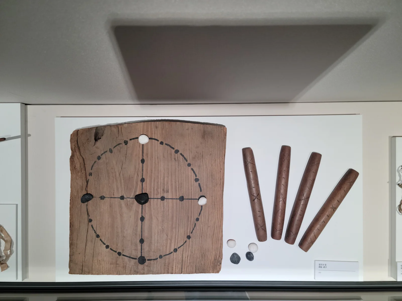 Historic wooden yutnori board with four wooden yut sticks and black and white playing tokens.