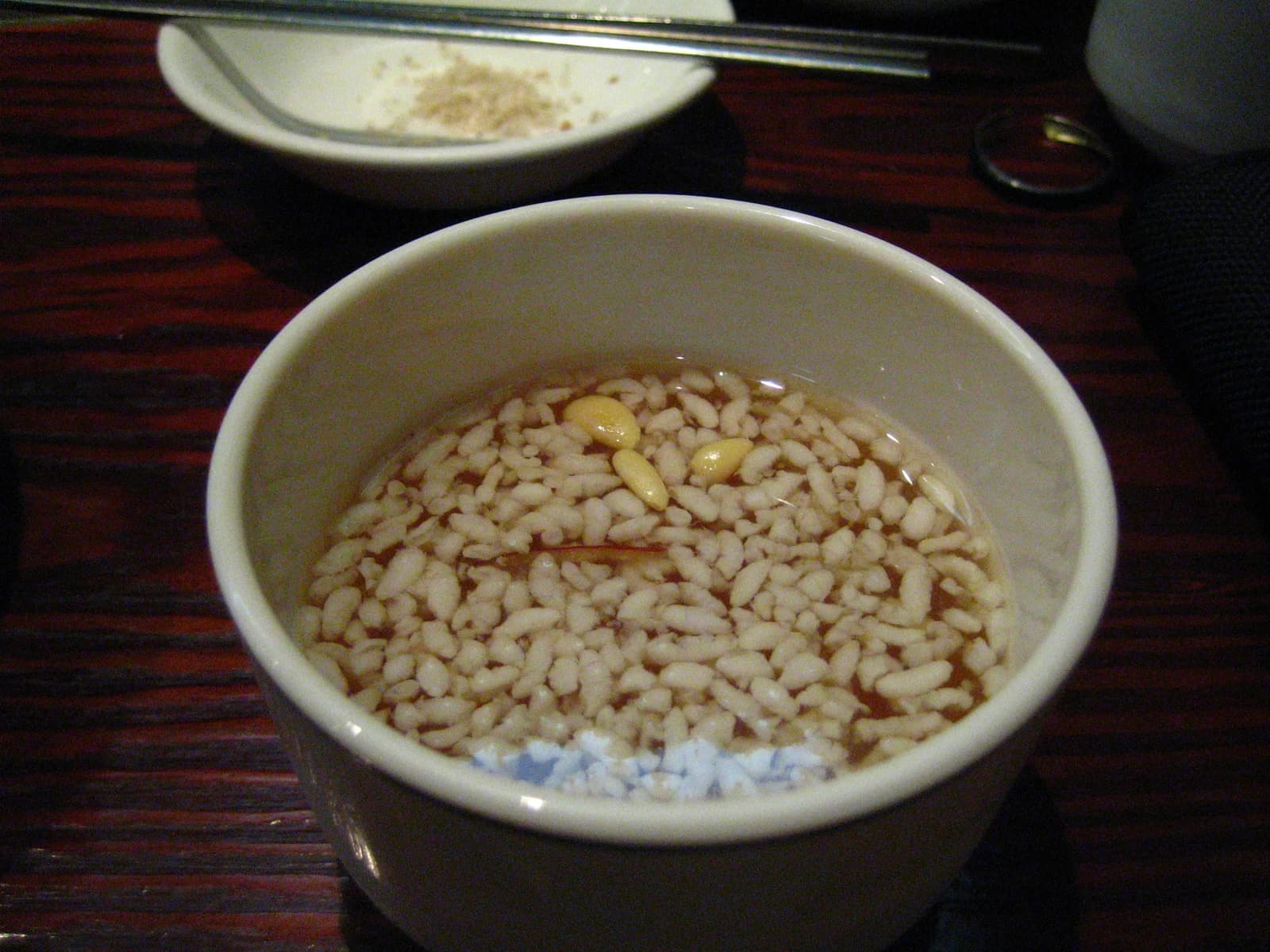 A bowl of sikhye with many visible rice grains and a few pine nuts on the surface