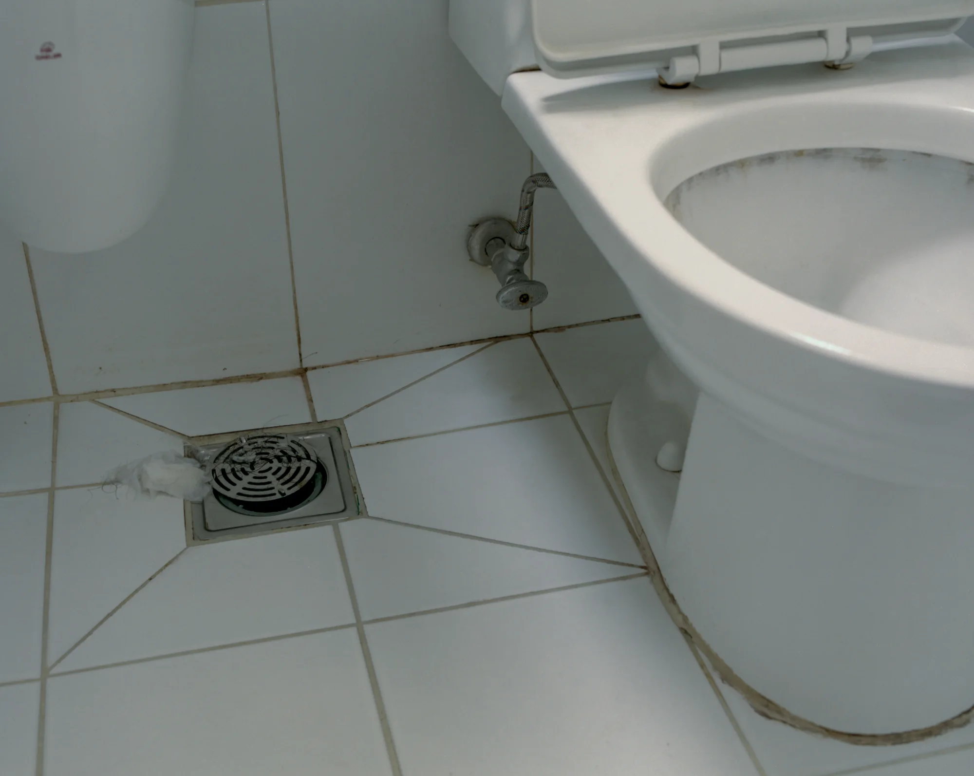 A floor drain set into the sloped tile floor beside a toilet