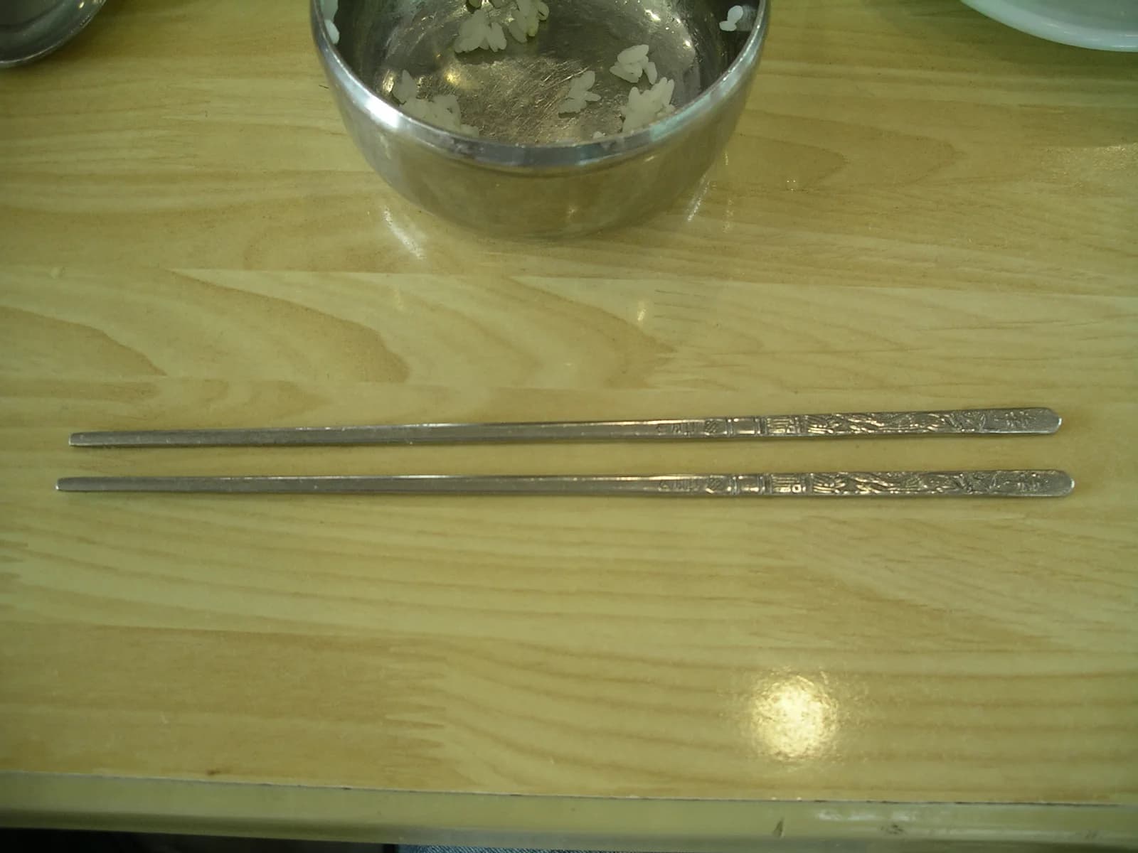 Flat stainless-steel Korean chopsticks held over a bowl