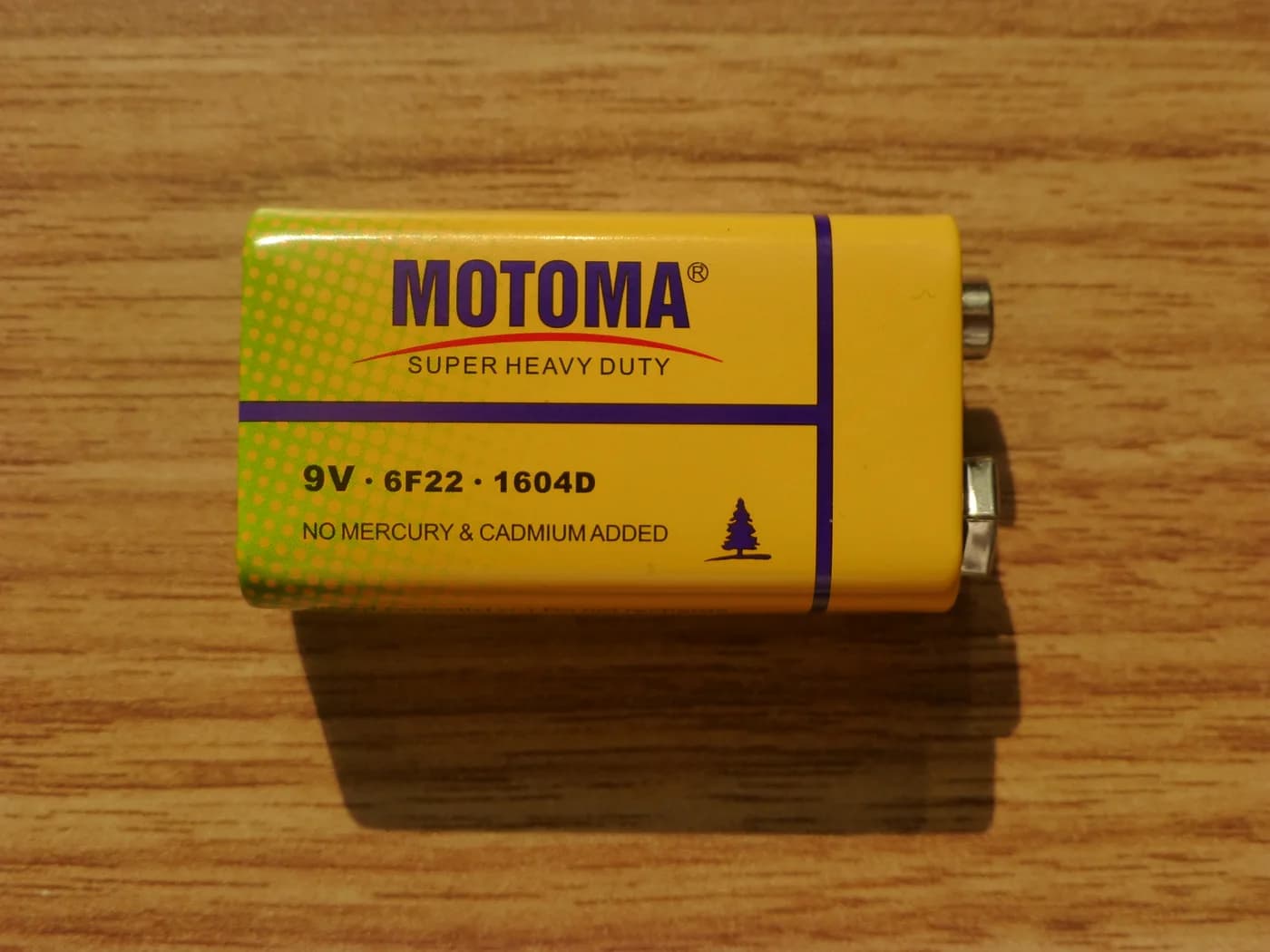 A rectangular 9-volt PP3 battery resting on a wooden surface