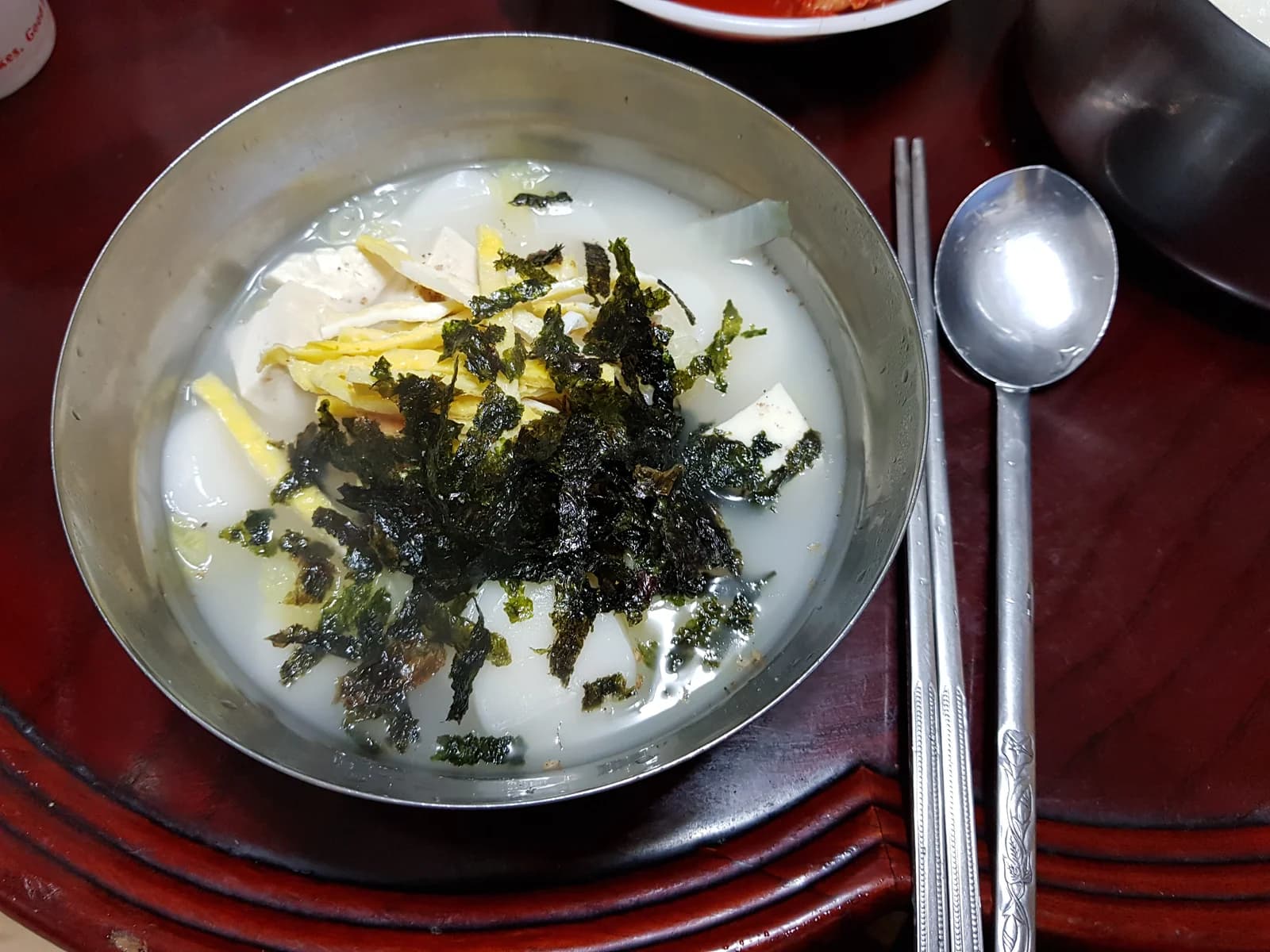 Tteokguk in a metal bowl with white rice-cake slices, egg strips and seaweed