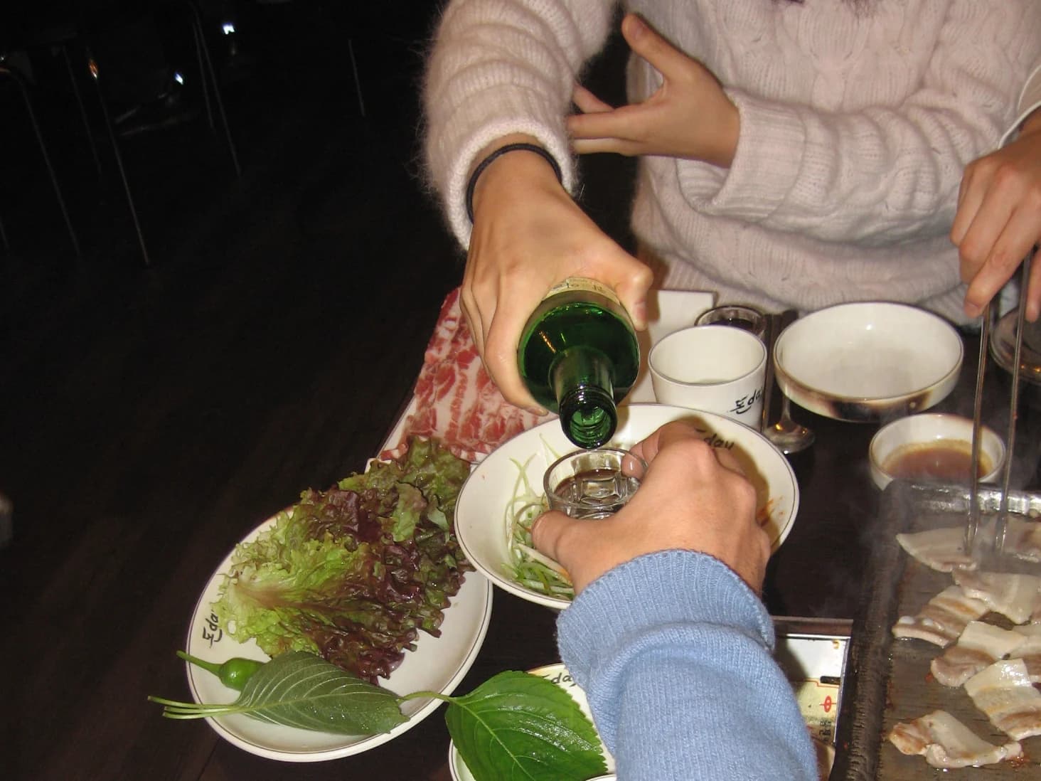 A diner pouring soju while the free hand supports the pouring forearm at a Korean meal