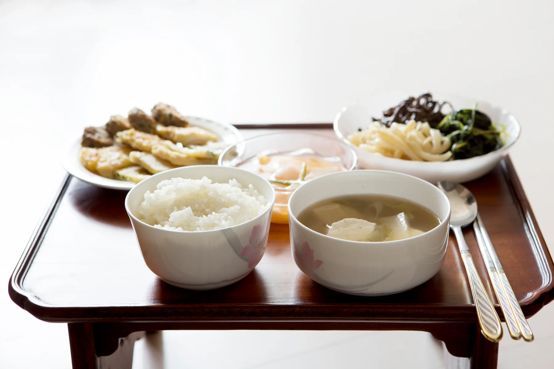A Korean meal with rice, soup and side dishes served on a low wooden bapsang table.